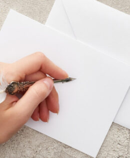 panoramic shot of woman writing on invitation card near weddings ring and eustoma flowers on textured surface